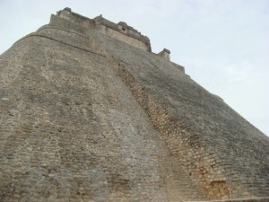The image shows a large, ancient stone structure with steep, sloping walls. The structure appears to be a pyramid or a similar type of monumental architecture, likely of historical or archaeological significance. The sky above is overcast.