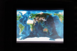 The image shows an in-flight entertainment screen displaying a world map with a flight path. The map highlights the current position of the airplane, which is shown as an airplane icon over the map. The map also indicates the areas of the world in daylight and darkness.
