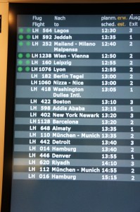 The image shows an airport departure board displaying flight information. The board lists various flights, their destinations, scheduled and estimated departure times, and the exit gates. Some of the destinations include Lagos, Jeddah, Milan, Vienna, Leipzig, Berlin, Nice, Washington, Boston, Addis Ababa, New York, Berkeley, Almaty, Detroit, Denver, Riyadh, Munich, and Hamburg. The flights are identified by their flight numbers, and some flights have green dots next to them, possibly indicating their status.