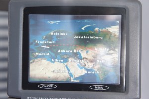 The image shows an in-flight entertainment screen displaying a flight path map. The map highlights various cities including Helsinki, Jekaterinburg, Frankfurt, Almaty, Madrid, Ankara, Baku, Athens, Damascus, Delhi, and Karachi. There is a small airplane icon indicating the current position of the flight, and a red dotted line representing the flight path. The screen has buttons labeled "ON/OFF" and "MENU" at the bottom.