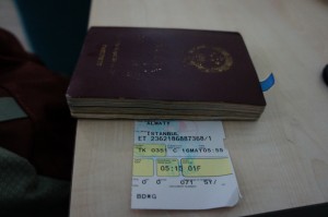 A maroon-colored passport is placed on a table with a boarding pass partially visible underneath it. The boarding pass has text indicating a flight from Istanbul and includes details such as the flight number, seat number, and departure time.