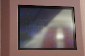 The image shows a screen displaying a map with several city names, including Budapest. The screen has a noticeable glare or reflection, making it difficult to clearly see all the details on the map. The screen is set within a pinkish frame.