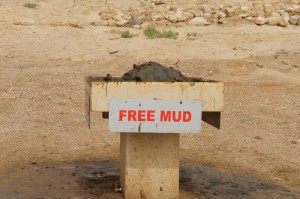 A concrete pedestal with a pile of mud on top and a sign attached to it that reads "FREE MUD" in red letters. The background is a dry, rocky area.