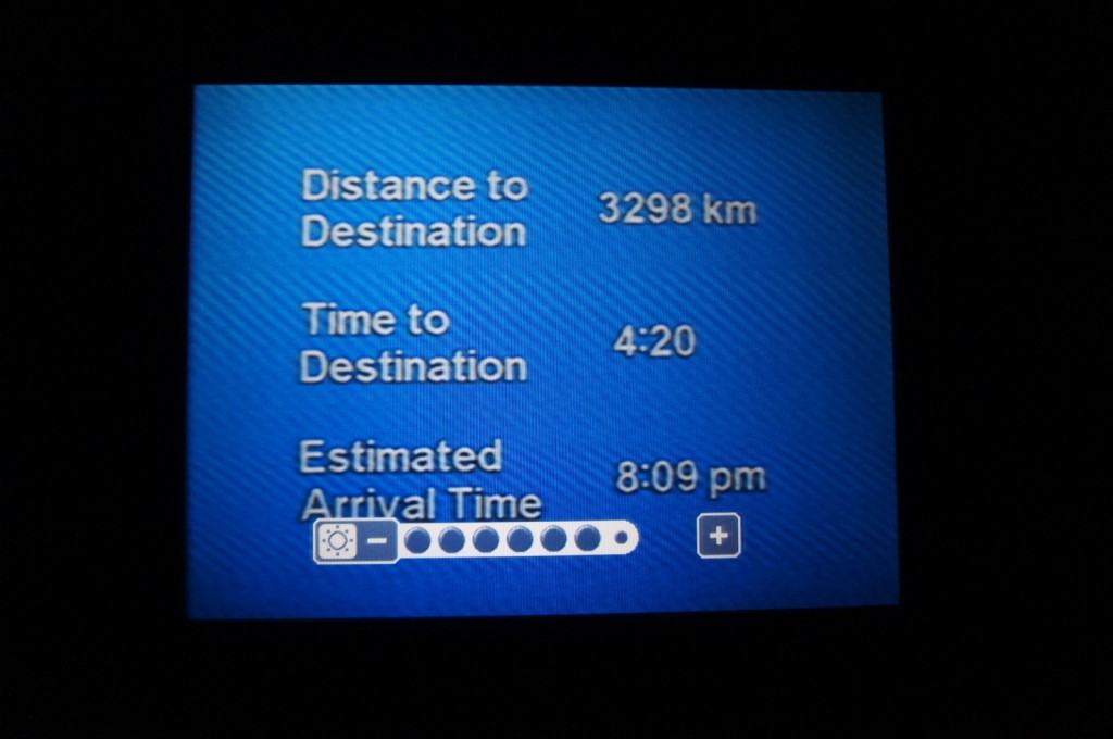 The image shows a screen with travel information. The details displayed are:
- Distance to Destination: 3298 km
- Time to Destination: 4:20
- Estimated Arrival Time: 8:09 pm
There is also a brightness adjustment bar at the bottom of the screen. The background of the screen is blue.