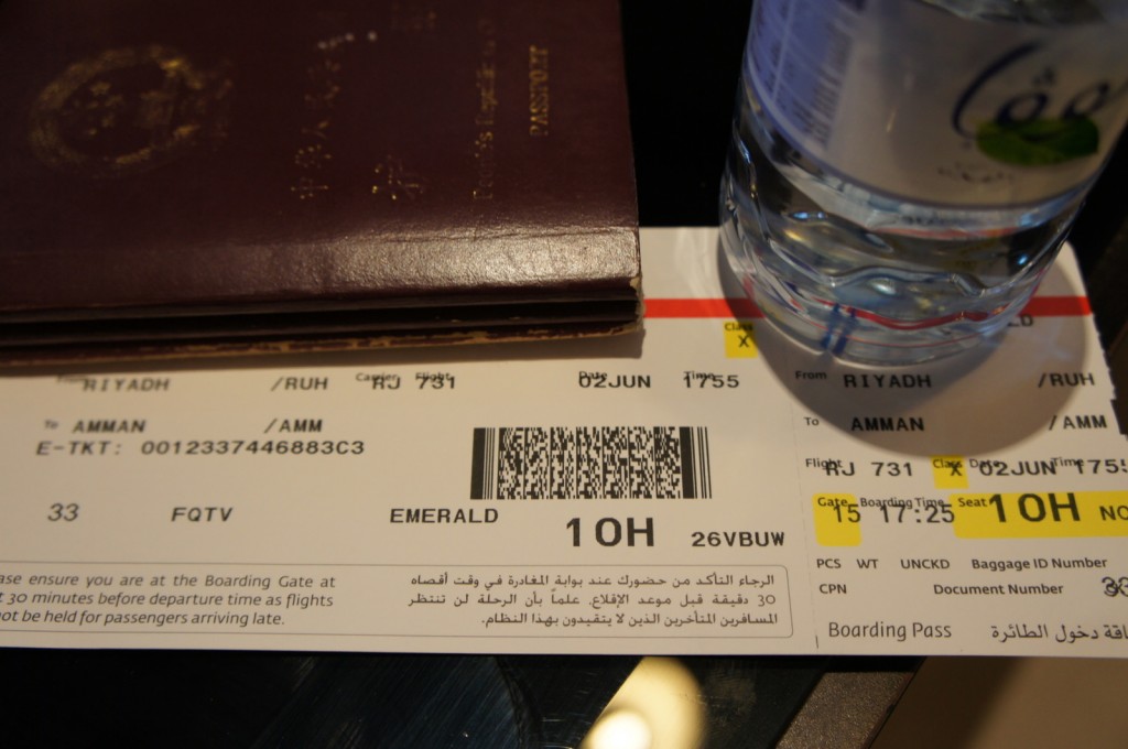 The image shows a close-up of a boarding pass, a passport, and a bottle of water. The boarding pass is for a flight from Riyadh (RUH) to Amman (AMM) on June 2nd, with a departure time of 17:55. The flight number is RJ 731, and the seat number is 10H. The boarding pass also includes a barcode and various other flight details. The passport is partially visible above the boarding pass, and the bottle of water is placed to the right of the boarding pass.