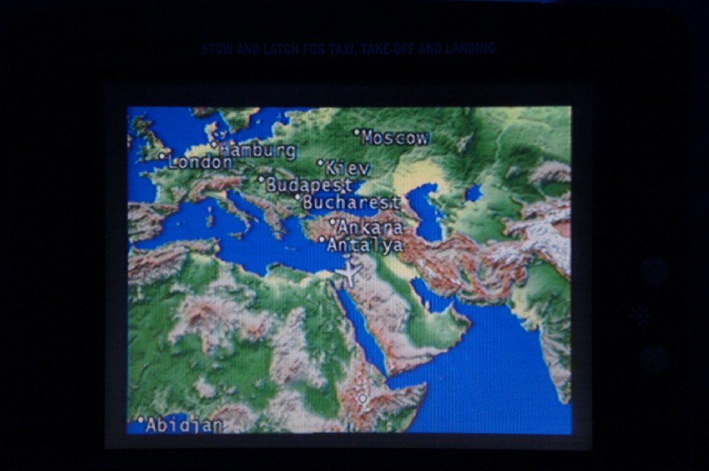 The image shows an in-flight entertainment screen displaying a map of Europe, the Middle East, and parts of Africa. Several cities are labeled on the map, including London, Hamburg, Kiev, Moscow, Budapest, Bucharest, Ankara, Antalya, and Abidjan. The map appears to be showing the flight path or location of an airplane, indicated by a small airplane icon near the center of the screen.