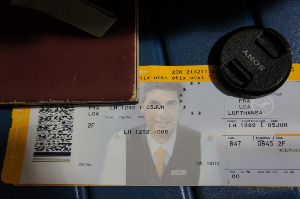 The image shows a Lufthansa boarding pass for flight LH 1292 from Frankfurt (FRA) to Larnaca (LCA) on June 5th. The boarding pass is for seat 2F, and the boarding gate is B47 with a boarding time of 08:45. The boarding pass is partially covered by a maroon-colored passport and a black Sony camera lens cap. The boarding pass also features a picture of a person in uniform, likely a pilot or flight attendant.