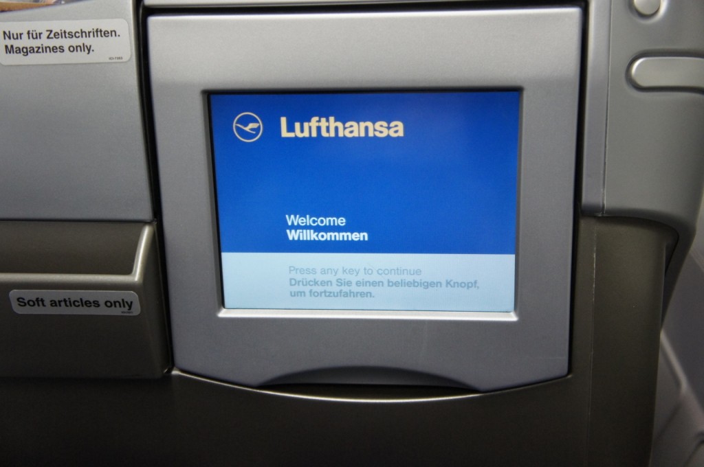 The image shows an in-flight entertainment screen on a Lufthansa airplane. The screen displays a welcome message in both English and German, with the text "Welcome" and "Willkommen." Below the welcome message, there is an instruction to "Press any key to continue" in both English and German. The Lufthansa logo and name are prominently displayed at the top of the screen. To the left of the screen, there are two labels: one reads "Nur für Zeitschriften. Magazines only." and the other reads "Soft articles only."
