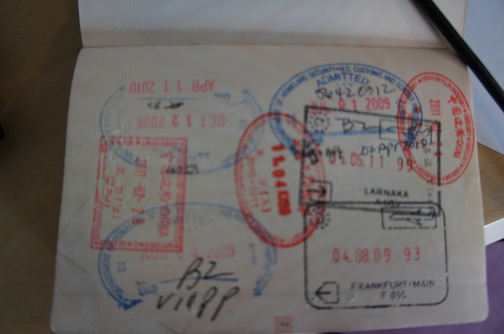 The image shows a page from a passport with multiple entry and exit stamps from various countries. The stamps are in different colors, including red, blue, and black, and contain various dates and locations. Some of the visible dates include October 1, 2009, April 11, 2010, and August 4, 1993. The stamps are overlapping and cover most of the page. There is also some handwritten text on the page.