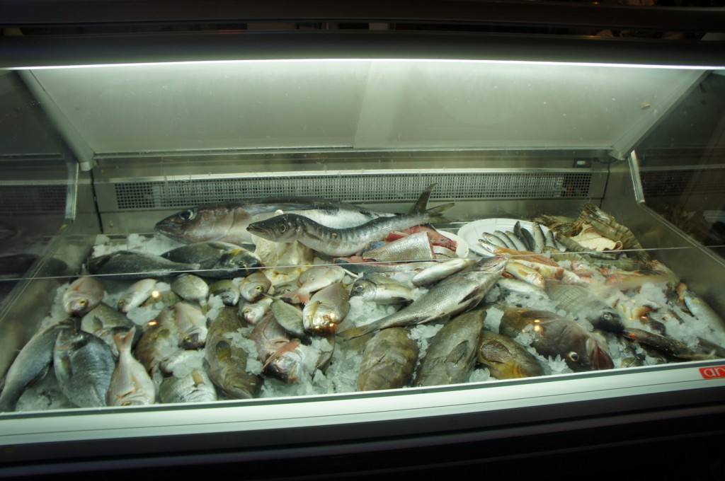 The image shows a display case filled with various types of fresh fish and seafood on a bed of ice. The fish are of different sizes and species, and the display is well-lit, likely in a market or seafood section of a store.