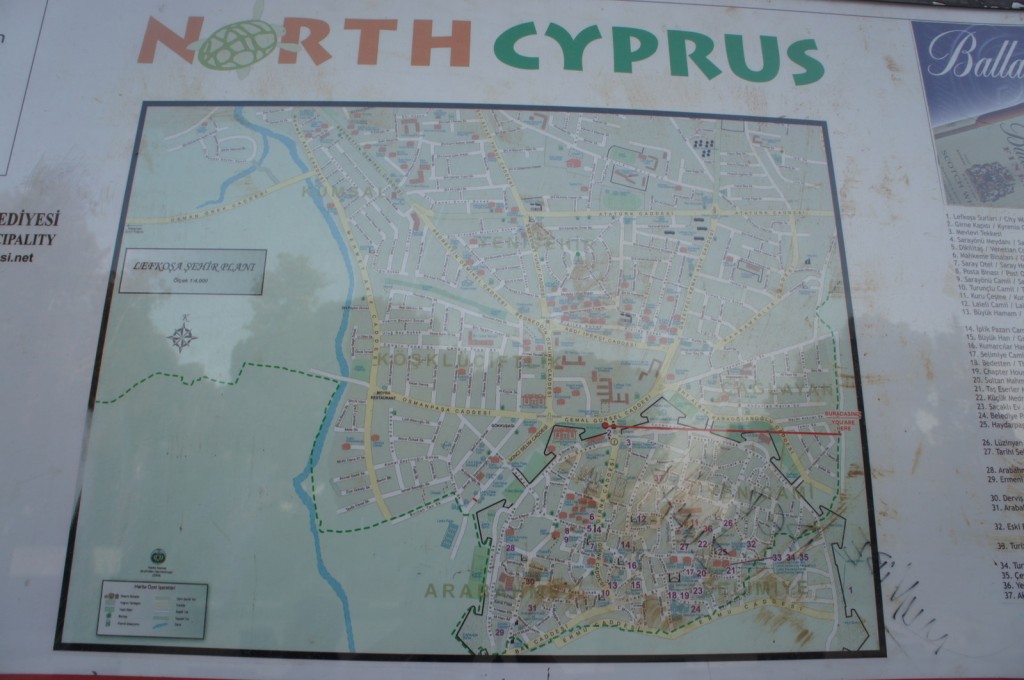 The image shows a detailed map of North Cyprus, specifically focusing on the city of Lefkoşa (Nicosia). The map includes various streets, landmarks, and points of interest, with labels and a legend for reference. The title "NORTH CYPRUS" is prominently displayed at the top of the map. There is also a compass rose indicating directions and a scale for distance measurement. The map is bordered by additional information and text on the left and right sides.