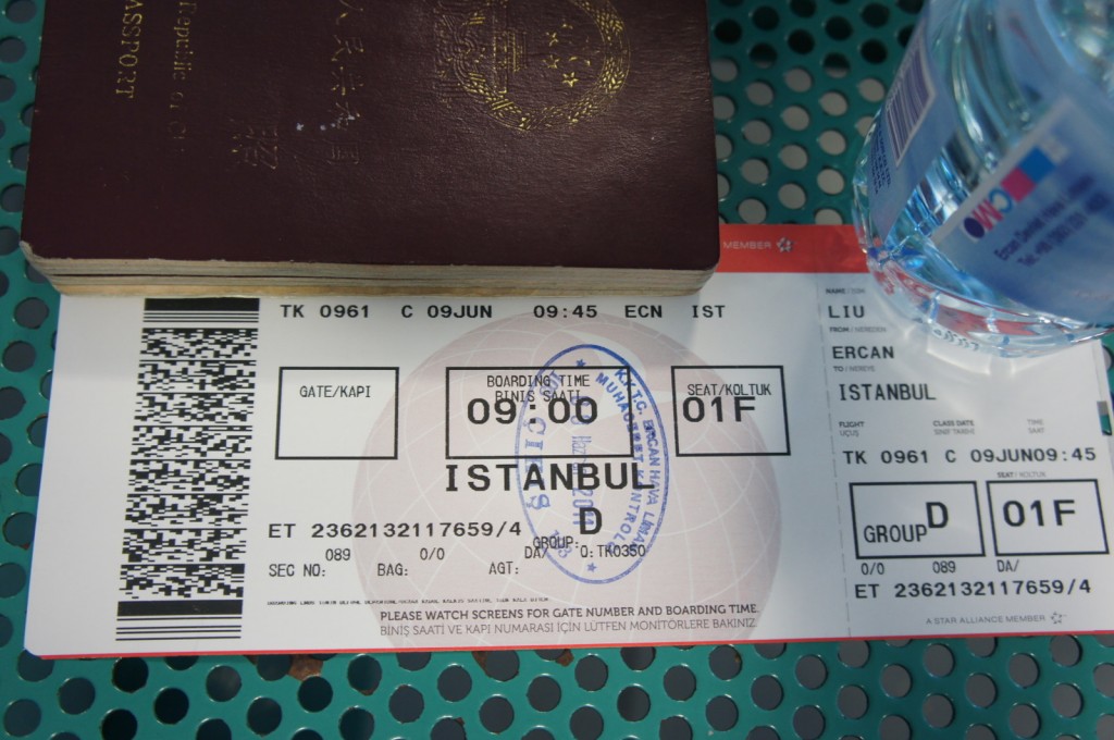 The image shows a close-up of a boarding pass for a flight from Ercan (ECN) to Istanbul (IST) on Turkish Airlines flight TK 0961. The boarding pass indicates a boarding time of 09:00 and a seat assignment of 01F in Group D. The boarding pass is placed on a perforated green surface, with a passport partially visible on top of it and a bottle of water to the right. The boarding pass also includes a barcode and various flight details.