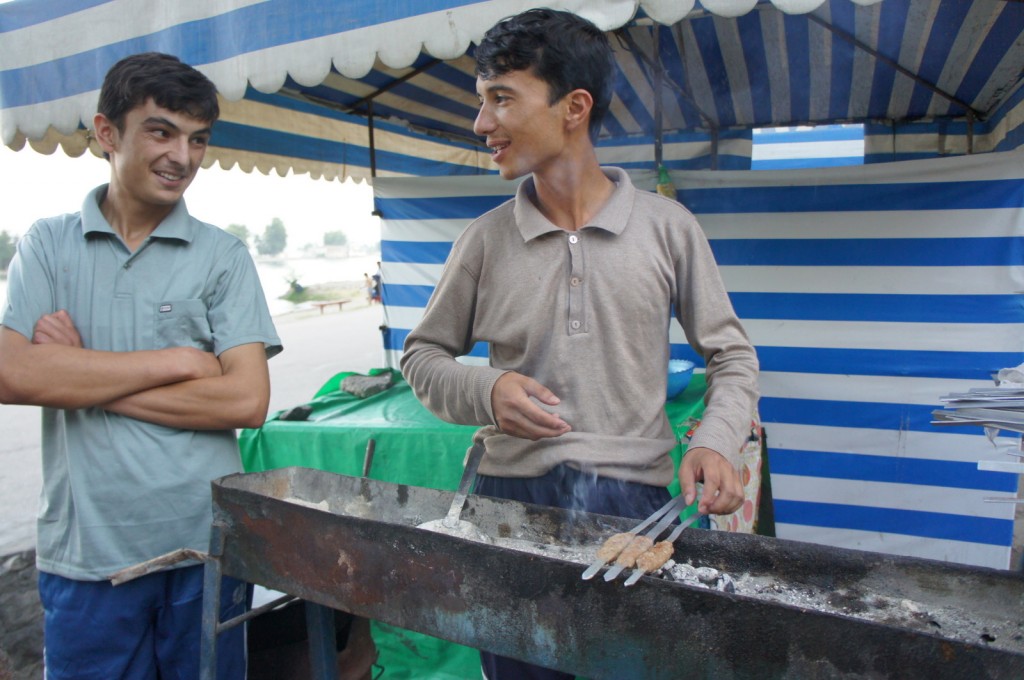 a couple of men cooking meat on a grill