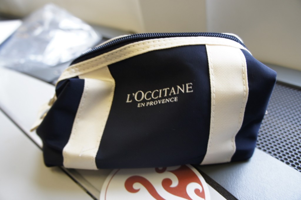 A small, navy blue and white zippered pouch with the text "L'OCCITANE EN PROVENCE" printed on it. The pouch is placed on a surface with a blurred background.
