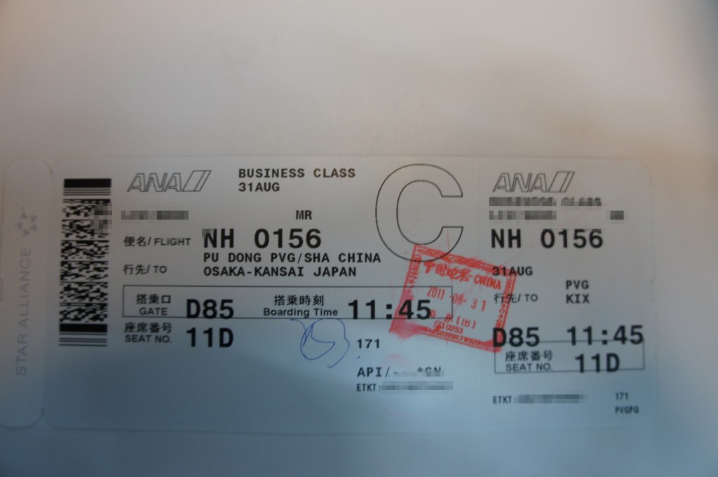 The image shows a business class boarding pass for an ANA (All Nippon Airways) flight. The flight number is NH 0156, departing on August 31st from Pu Dong (PVG/SHA) in China to Osaka-Kansai (KIX) in Japan. The boarding gate is D85, and the boarding time is 11:45. The seat number is 11D. There is a red stamp on the boarding pass, and some text is blurred for privacy. The boarding pass also features a barcode and the Star Alliance logo.