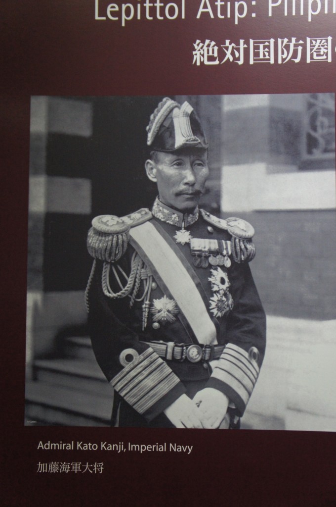 The image is a historical black-and-white photograph of Admiral Kato Kanji of the Imperial Navy. He is dressed in a formal military uniform adorned with various medals and decorations. The background includes text in both English and Japanese. The English text reads "Admiral Kato Kanji, Imperial Navy," and the Japanese text is written below it. The upper part of the image contains additional text in both English and Japanese.