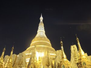 a large gold building with a pointed top with Shwedagon Pagoda in the background