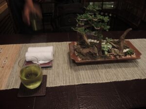 a table with a bonsai tree and a glass of water