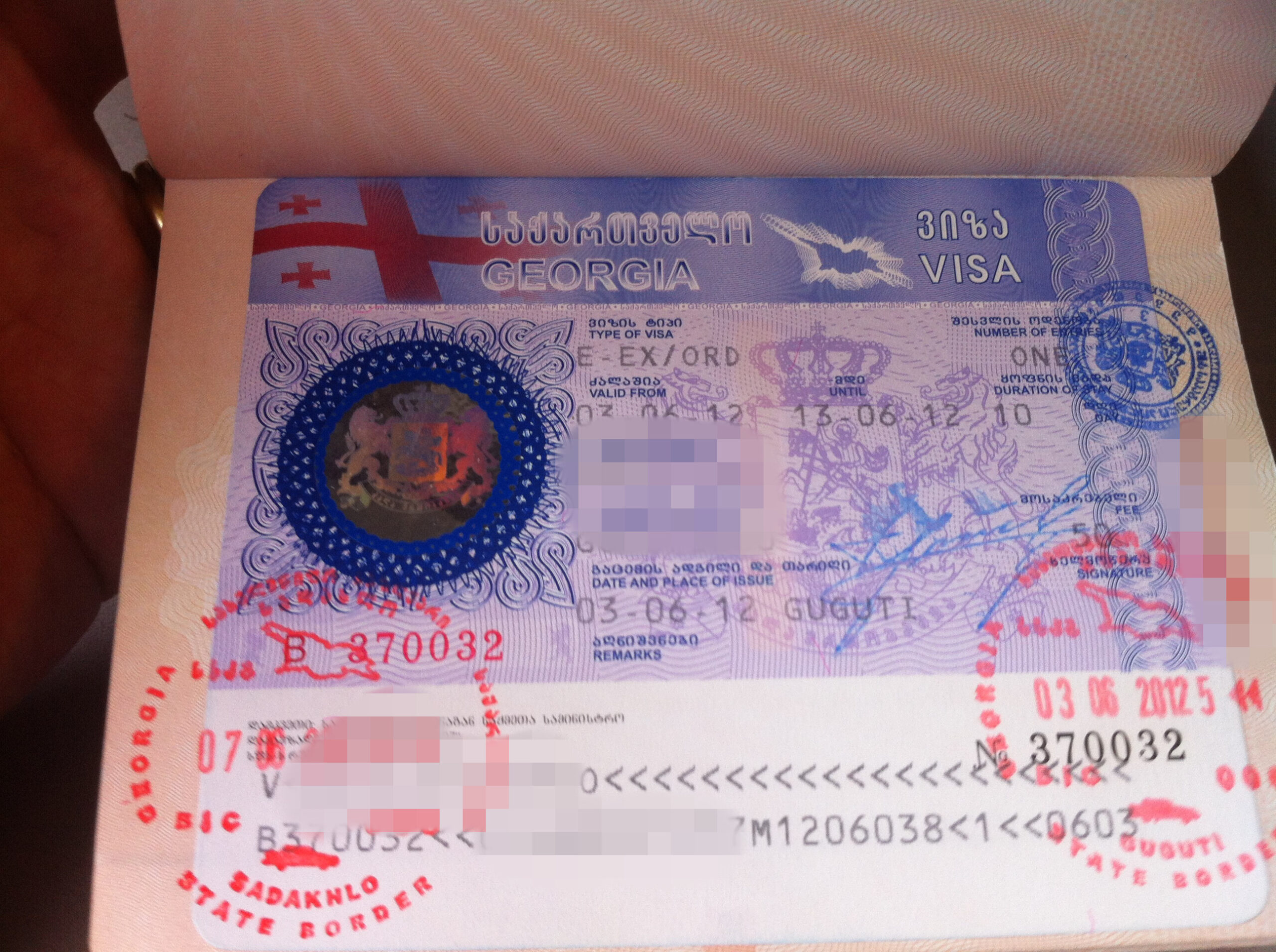 The image shows a Georgian visa affixed to a passport page. The visa includes various details such as the type of visa, validity dates, and place of issue. There are also several stamps and a holographic security feature. The text on the visa is in both Georgian and English. Some personal information is blurred out for privacy.