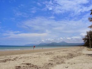 a sandy beach with blue water and clouds