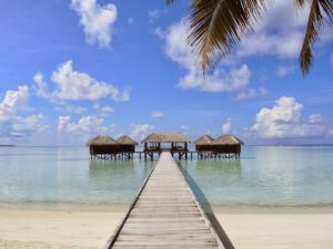 a dock leading to a beach with huts on the water