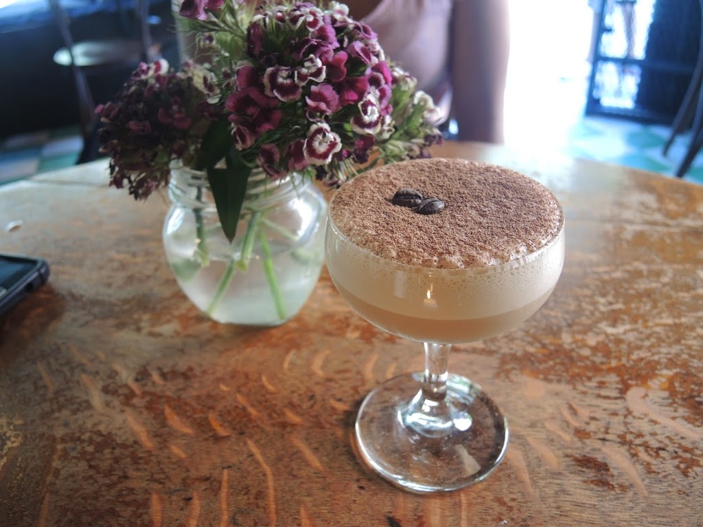 a drink in a glass next to a vase of flowers