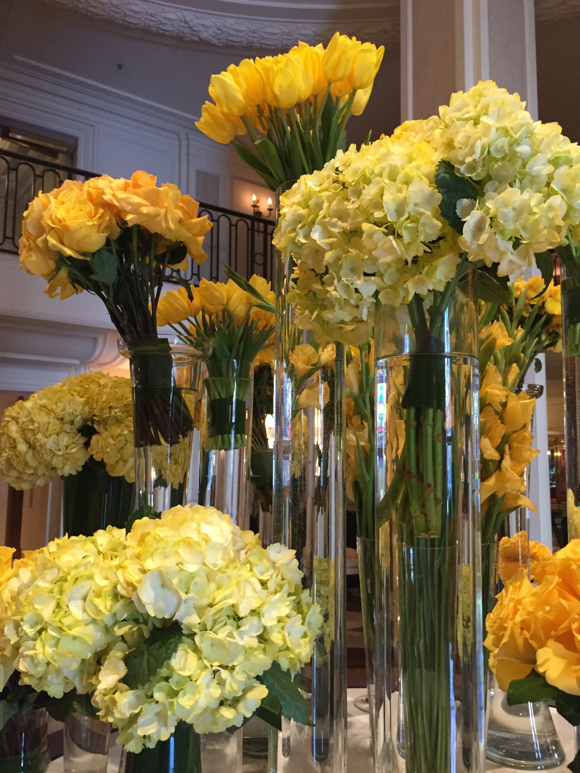 a group of yellow flowers in tall glass vases