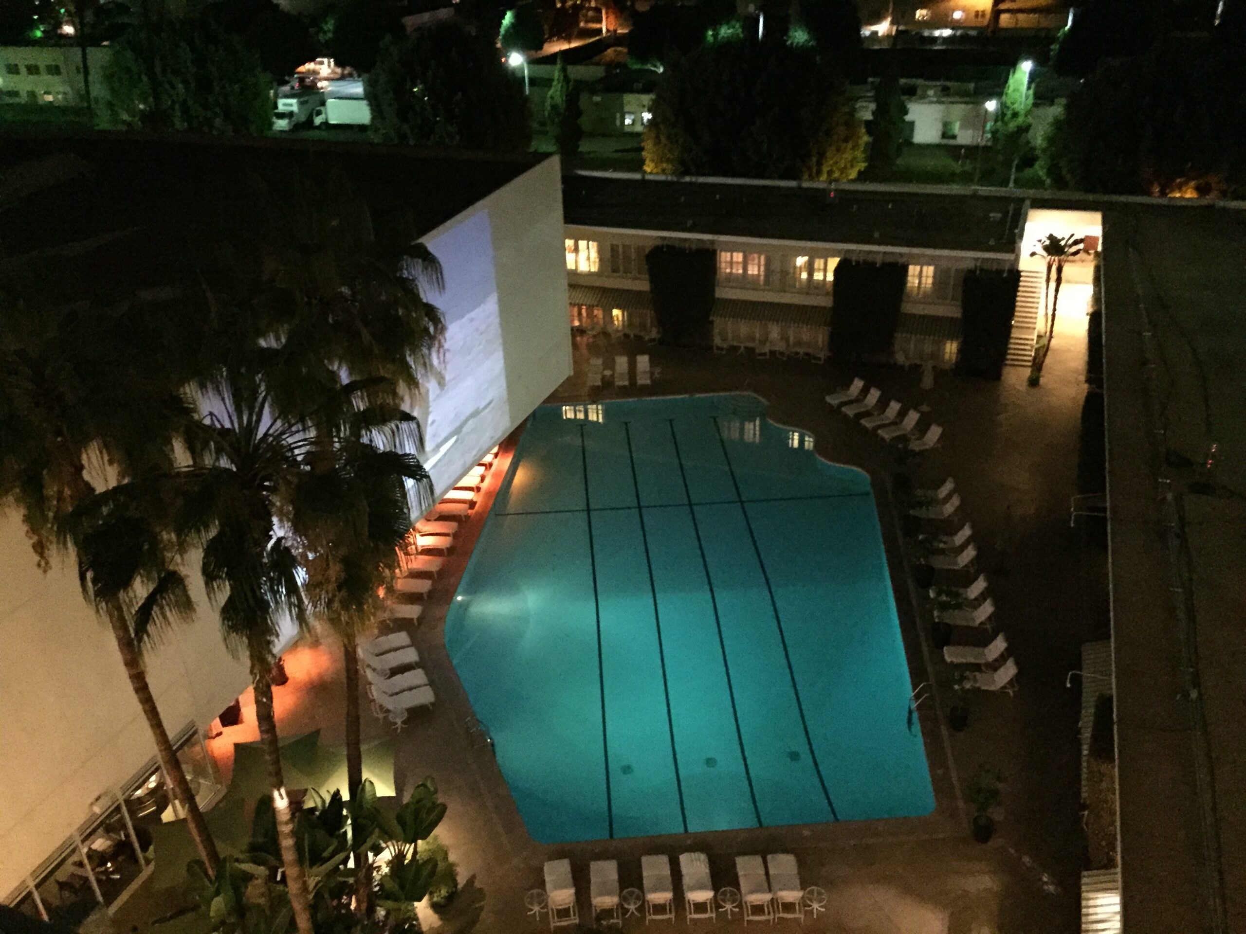 a swimming pool with palm trees and a building at night
