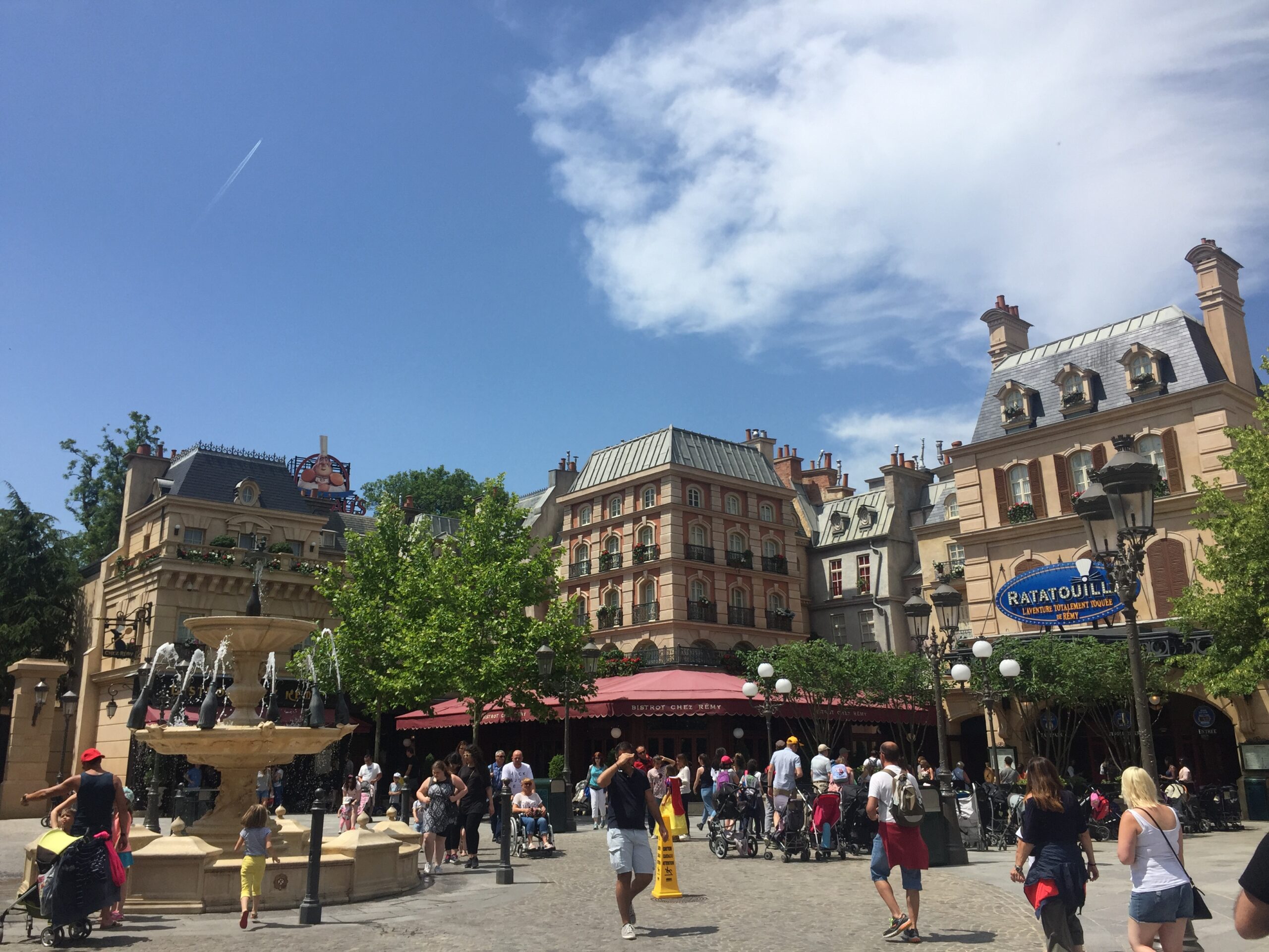 a group of people in a courtyard with a fountain and buildings