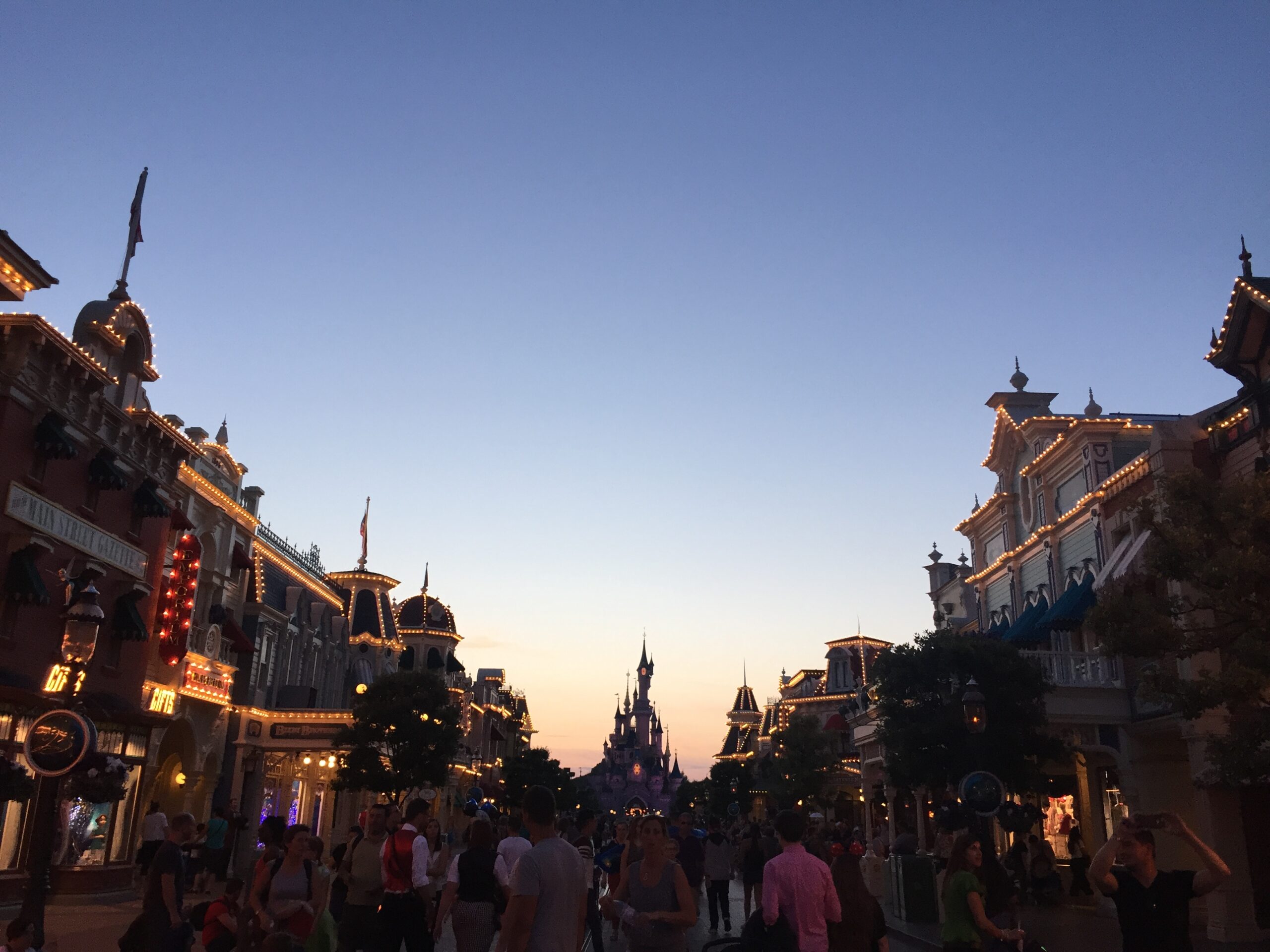 a crowd of people walking down a street with buildings and a castle in the background