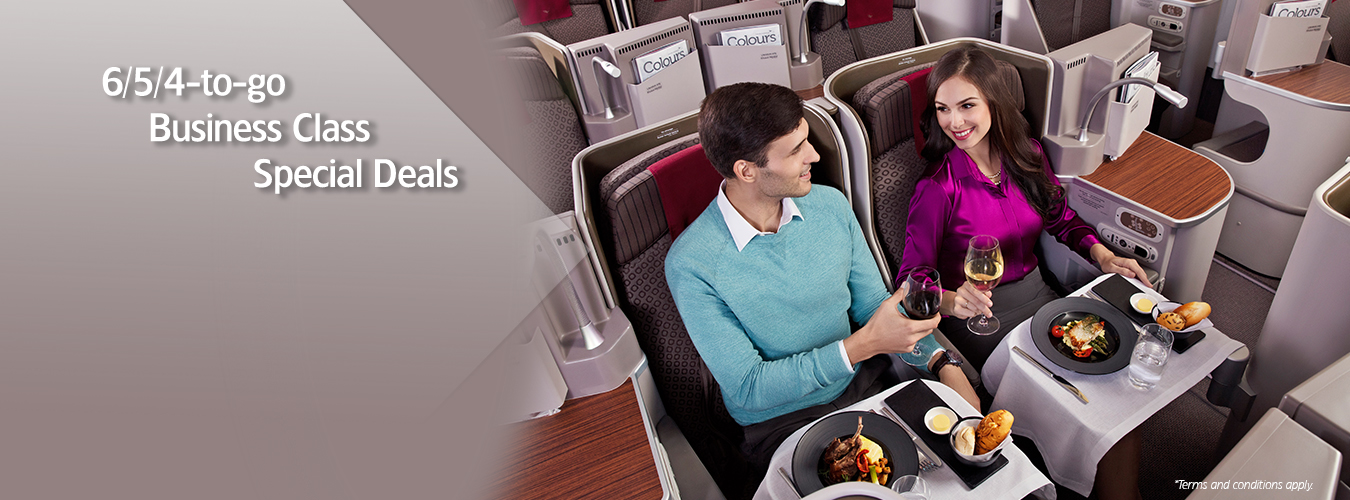 Alt text: A man and a woman are seated in business class on an airplane, enjoying a meal and drinks. The man is wearing a light blue sweater, and the woman is wearing a purple blouse. They are smiling and clinking their wine glasses. The seats are spacious with individual screens and ample legroom. The left side of the image has text that reads "6/5/4-to-go Business Class Special Deals."